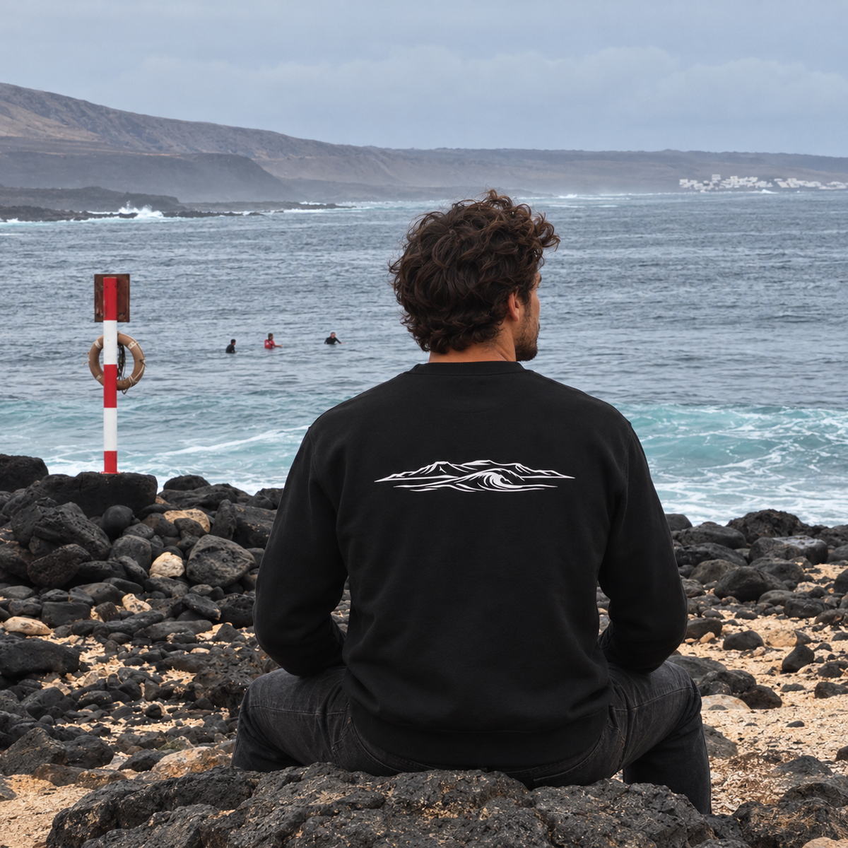 Sudadera negra Ocean and Fire, vista trasera sentado frente al mar